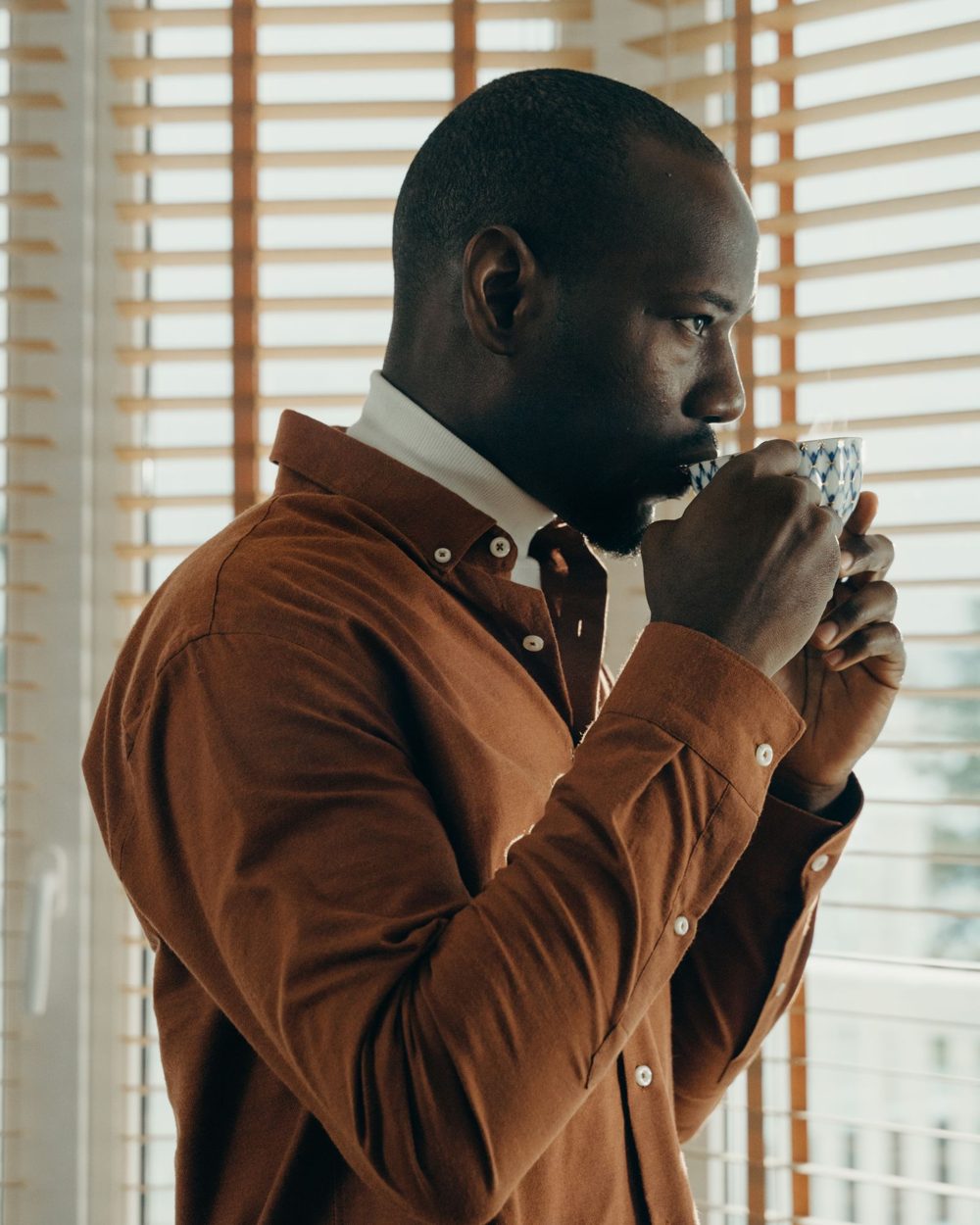 Man drinking a cup of herbal tea by a window