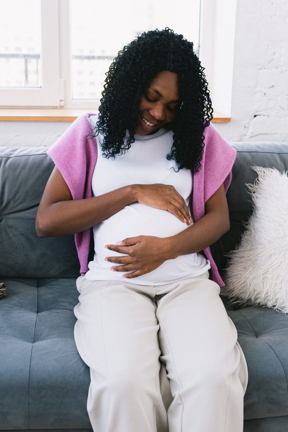 Pregnant woman smiling and holding her belly on a sofa